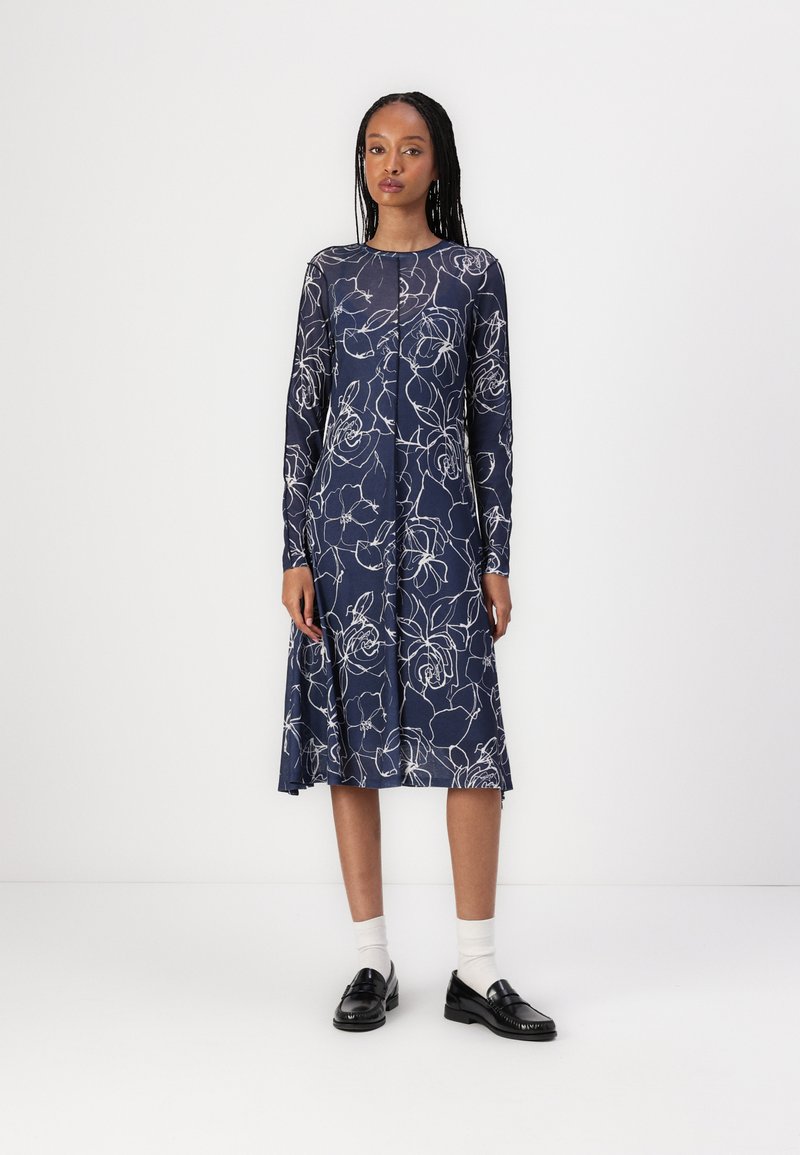 Vestido de marinero con estampado floral blanco, mangas largas, escote redondo y dobladillo acampanado. Lleva unos mocasines negros y calcetines blancos.