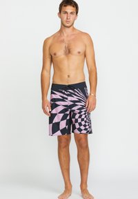 Pantaloni da bagno neri e rosa con un design a spirale, realizzati in materiale ad asciugatura rapida; dotati di vita elasticizzata e cordoncino.