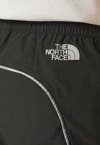 Mustat urheilushortsit, jotka on valmistettu kevyestä materiaalista. Niissä on erottuva harmaa reunus ja kyljessä "THE NORTH FACE" -logo.