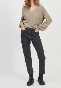 Pull côtelé beige avec col en V, associé à un jean noir taille haute à jambes droites et à des bottines noires. Look simple et décontracté.