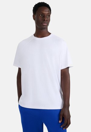 Biała bawełniana koszulka z krótkimi rękawami i okrągłym dekoltem, o luźnym kroju i raglanowym fasonie rękawów. Gładka faktura, bez wzorów.