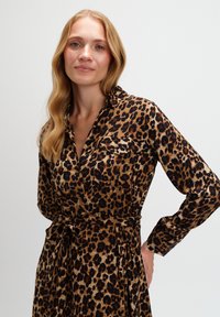 Sukienka w panterkę z długimi rękawami, kołnierzykiem, dwoma kieszeniami na piersi oraz paskiem w talii, w odcieniach brązu i czerni, uszyta z miękkiego, teksturowanego materiału.