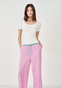 Biała, dopasowana bluzka z krótkim rękawem i okrągłym dekoltem, zestawiona z luźnymi różowymi spodniami w wzory z turkusowym sznurkiem ściągającym i pasem.
