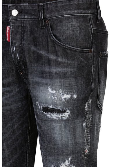 Jeans in denim nero usurato con finitura sbiadita, numerosi strappi e cuciture in contrasto, con un'etichetta del marchio sulla vita.