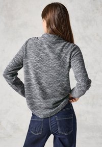 Graues, strukturiertes Strickshirt mit langen Ärmeln und einem Kragen, kombiniert mit dunkelblauen Jeans aus Denim mit Gesäßtaschen und kontrastierenden Nähten.