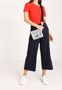 Červený krátký top s krátkým rukávem ve spojení s tmavě modrými culottes s proužky a bílými teniskami. Outfit doplňuje stříbrná kabelka přes rameno.