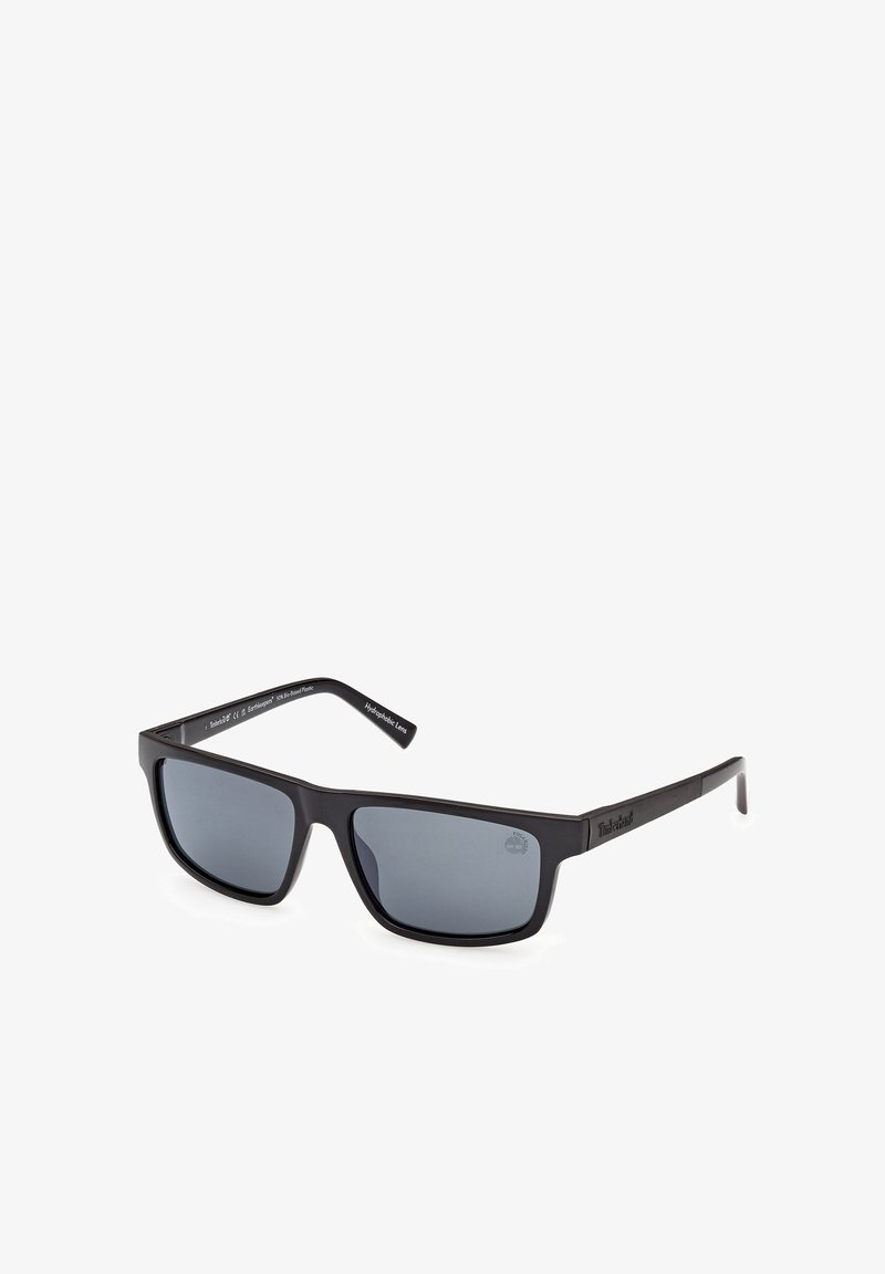 Lunettes de soleil Timberland rectangulaires noires avec verres polarisés foncés et branches fines sur fond blanc.