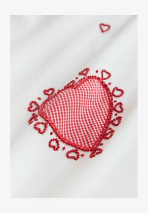 Biela tkanina s červeným kockovaným dizajnom srdca, obklopená zložitou červenou výšivkou s malými srdiečkami pozdĺž okrajov.