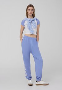 T-shirt corta di colore azzurro chiaro con maniche corte e dettagli bianchi, abbinata a pantaloni jogger azzurro chiaro con la scritta "NEW YORK".