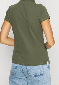 Olivgrön kortärmad polo med klassisk krage, texturerad tyg och sidslitsar, kombinerad med ljusblå denimshorts.