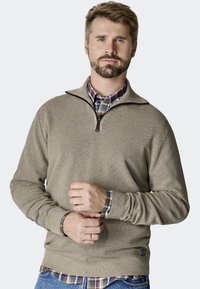 Beżowy sweter z półsuwnym kołnierzem, z teksturowanej tkaniny i prążkowanymi mankietami. Nosi się go na koszuli w kratę, o luźnym kroju, z detalami w postaci przeszyć.