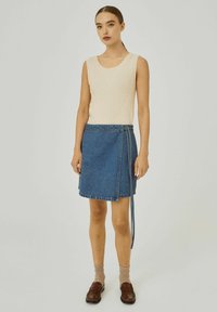 Beige geribbelde tanktop met een ronde hals, gecombineerd met een blauwe denim wikkelrok met een gestrikt riem en een zoom boven de knie.