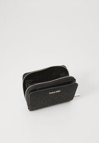 Fekete bőr pénztárca texturált mintával. Ezüst cipzárral és Calvin Klein logóval az elején. Belsejében több kártyatartó található.