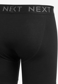 Pantaloni scurți negri din material elastic, cu o textură moale, având o talie largă de marcă, pe care este inscripționat "NEXT" cu litere gri.