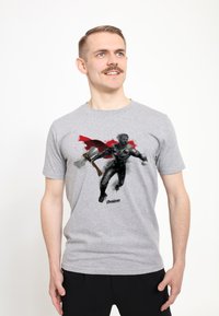 Camiseta de algodón gris con un gráfico de un personaje con armadura, llevando una capa roja y sosteniendo un hacha, con el texto "Avengers" en la parte inferior.