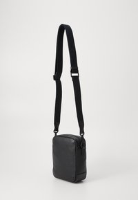 Bolso crossbody de cuero negro con un acabado texturizado, forma rectangular y correa de nylon ajustable. Cuenta con un cierre superior con cremallera.