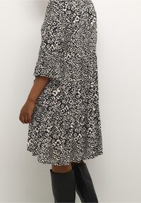 Zúžené šaty s černobílým leopardím potiskem. Mají krátké rukávy, vrstvený design a lehký materiál. Stylizováno s černými vysokými botami po kolena.