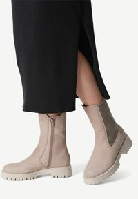 Beige enkellaarzen met een zijrits, elastische panelen en een gestructureerde zool. Het ontwerp heeft een slanke silhouette en een minimalistische esthetiek.