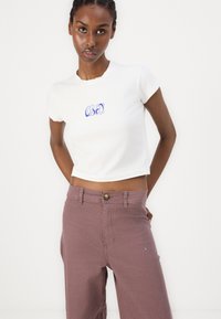 White cropped t-shirt with a blue "OBEY" graphic, paired with light purple high-waisted pants featuring a front button closure.