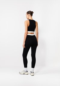 Čierny set športového oblečenia s bezrukávovým skráteným topom a legínami s vysokým pásom a bielym elastickým pásom. Mäkko, pružné tkaniny a priliehavý strih.