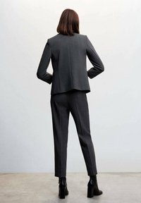 Blazer gris ajustado y pantalones a juego en una tela elegante, combinados con botas de tobillo negras. Vista desde atrás, fondo liso.