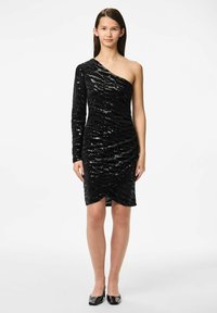 Juoda vieno peties suknelė, pagaminta iš tekstūruoto blizgučių audinio, su susiraukšlėta konstrukcija ir asimetrišku hemu. Turi ilgą rankovę ir prigludusią siluetą.