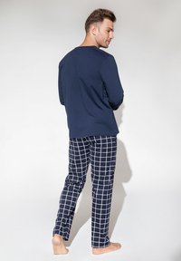 Granatowa bluzka z długim rękawem i czarne spodnie do pizamy z białym wzorem w kratę. Miękka tkanina, luźny krój i długość do kostek.