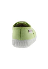 Zapatilla de lona verde con suela de goma blanca, que presenta un patrón de agarre texturizado. La vista trasera muestra la etiqueta del logo en el lateral.