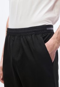 Κοντινό πλάνο ατόμου που φοράει μαύρο παντελόνι με ελαστική μέση, με το χέρι στην τσέπη και ένα λευκό πουκάμισο κρυμμένο μέσα.