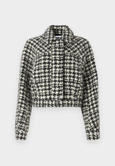 Korte jacket met een zwart-wit pied-de-poule patroon, gemaakt van textuurstof. Heeft een kraag en lange mouwen, met een rits aan de voorkant.