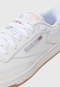 Baskets en cuir blanc avec semelle en caoutchouc texturée, bout rond et design à lacets. Présente le logo Reebok avec un accent du drapeau Union Jack.