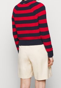 Sweter dziany w czerwone i granatowe paski, z prążkowanym dekoltem i mankietami. W połączeniu z beżowymi szortami.