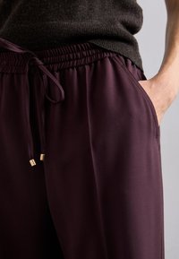Bordeauxkleurige broek met een tailleband met trekkoord, voorzien van gouden hardware accenten. Zachte stof met een gladde textuur en zijzakken.