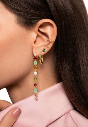 Pendientes de oro colgantes con piedras preciosas de colores rojo, verde, azul, amarillo y blanco. Presentan un aro de oro y aros de oído, llevados sobre una tela rosa.
