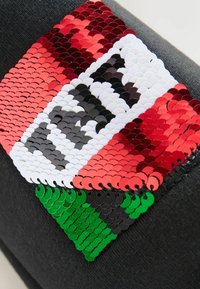 Black fabric featuring a multi-colored sequin patch with red, white, black, and green sections arranged in a geometric design.