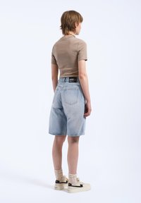 Shorts de mezclilla azul claro con un corte relajado, que presentan una cintura de altura media y bolsillos traseros. Combinados con una blusa ajustada de manga corta beige.