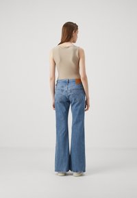 Un body sans manches beige associé à un jean en denim bleu clair à jambes larges, comportant une patch à l'arrière, présenté de dos.
