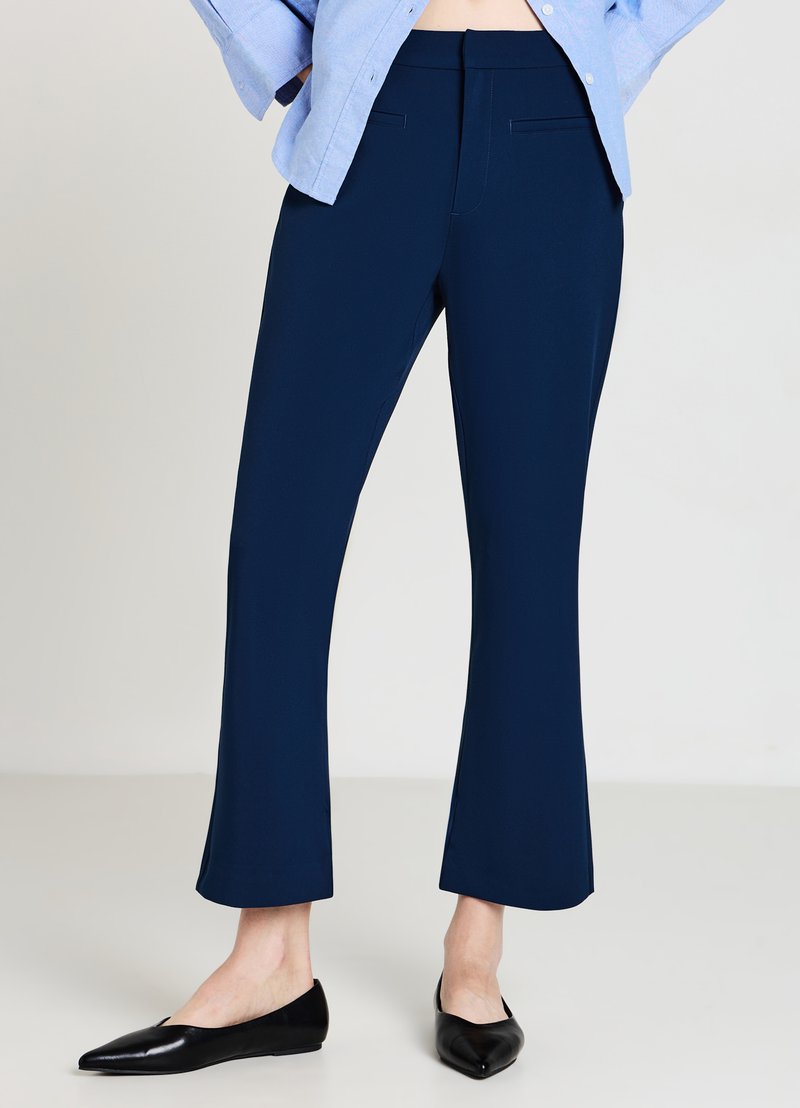 Pantalon taillé bleu marine avec un ourlet évasé, fait d'un tissu lisse. Comprend deux poches avant et une taille ajustée.