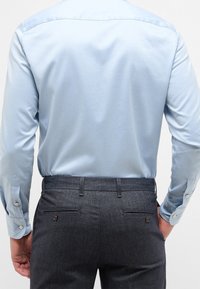 Lichtblauwe overhemd met lange mouwen en een gladde textuur, gecombineerd met donkergrijze broek met twee achterzakken en subtiele hardware-accenten.