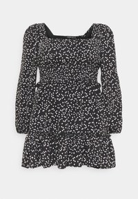 Svart klänning med långa ärmar, fyrkantig halsringning, smockad midja och flerlagers volangslut. Har ett vitt hjärt-mönster över hela.