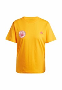 Žluté bavlněné tričko s kulatým červeným logem na levé části hrudi a malým růžovým logem Adidas na pravém rameni. Krátké rukávy.