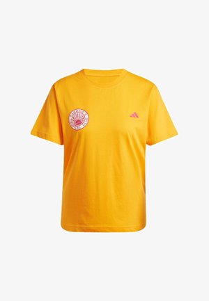 Camiseta de algodón amarilla con un logo circular rojo en el lado izquierdo del pecho y un pequeño logo de Adidas en rosa en el hombro derecho. Manga corta.