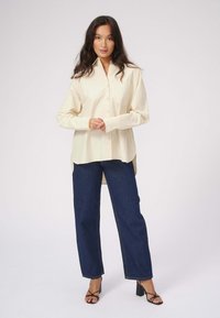 Cremefarvet skjorte med knapper og lange ærmer, parret med mørkeblå brede jeans. Sorte strophæle fuldender outfittet.