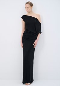 Sort off-shoulder kjole med en tætsiddende silhuet, samlet tekstur ved taljen og gulvlængde design. Har en subtil glans og blødt stof.