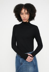 Fekete, hosszú ujjú, magasnyakú felső, testhez simuló fazonban. Az anyaga simának tűnik, farmerkabáttal párosítva, laza stílust sugall.