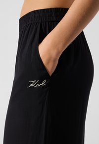 Pantalon noir en matière légère avec une ceinture élastique, doté d'une poche latérale et d'un logo "Karl" brodé en blanc.
