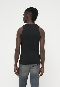 Μαύρο αμάνικο τοπ από ριμπ ύφασμα, εφαρμοστό σχέδιο, μονόχρωμη υφή. Φοριέται με ανοιχτό γκρι τζιν παντελόνι.