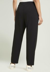 Pantalones negros de tiro alto, corte relajado, con cintura elástica, con una textura suave y diseño de pierna recta, combinados con zapatos plateados.
