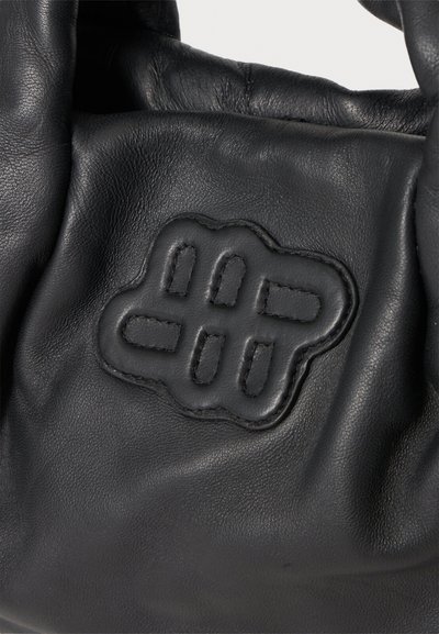 Gros plan d'un sac en cuir noir avec un détail de logo abstrait cousu sur sa surface.