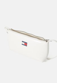 White faux leather clutch bag with a top zip closure, featuring a logo patch in blue, red, and white. Smooth texture and slim design.